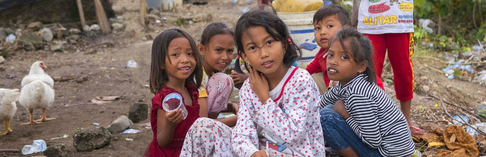 A group of seven young children are gathered in a space littered with branches, blankets and trash. When their homes were destroyed in the 2018 Indonesia earthquake and tsunami, theylived in a temporary shelter and survived on supplies provided by Save the Children and other aid organizations. Photo credit: Ardiles Rante / Save the Children, Oct 2018.