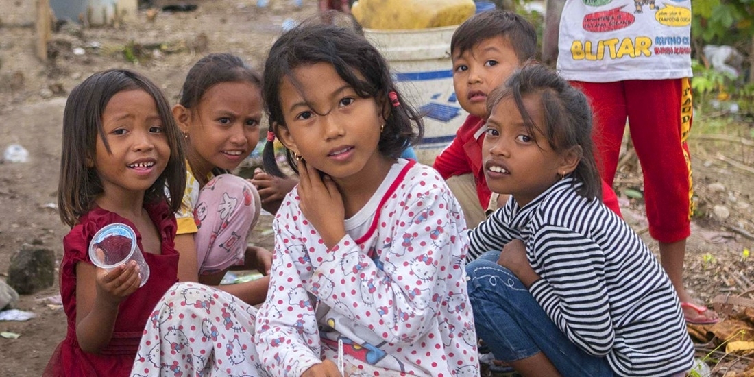 A group of seven young children are gathered in a space littered with branches, blankets and trash. When their homes were destroyed in the 2018 Indonesia earthquake and tsunami, they lived in a temporary shelter and survived on supplies provided by Save the Children and other aid organizations. Photo credit: Ardiles Rante / Save the Children, Oct 2018.