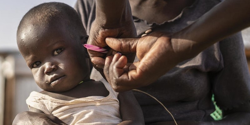 A little boy sits in the lap of his mother who holds onto his small hand as a health worker screens him for illness, including malnutrition. A community health volunteer in Kenya diagnosed the little boy and gave him the antibiotics and highly nutritious food he needed to begin his recovery. Photo credit: Fredrik Lerneryd / Save the Children, July 2019.