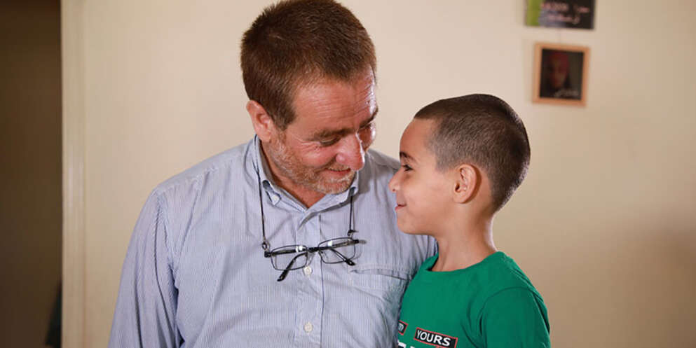Farid and his son stand next to and look toward each other, smiling.