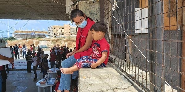 A Save the Children staff member sits with a child on a wall in Lebanon