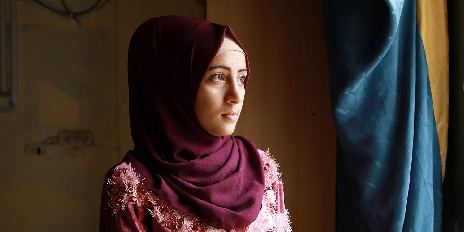 Lebanon, a teenage Syrian refugee girl in a burgundy hijab looks out a window