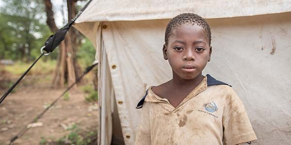 A ten-year old African child who lost his home when Cyclone Idai hit stands near a tent in Mozambique.