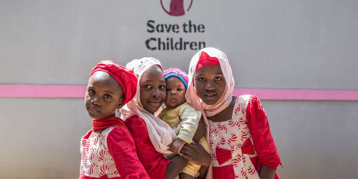 A group of four siblings, including a baby, stand together outside a health clinic in Nigeria.
