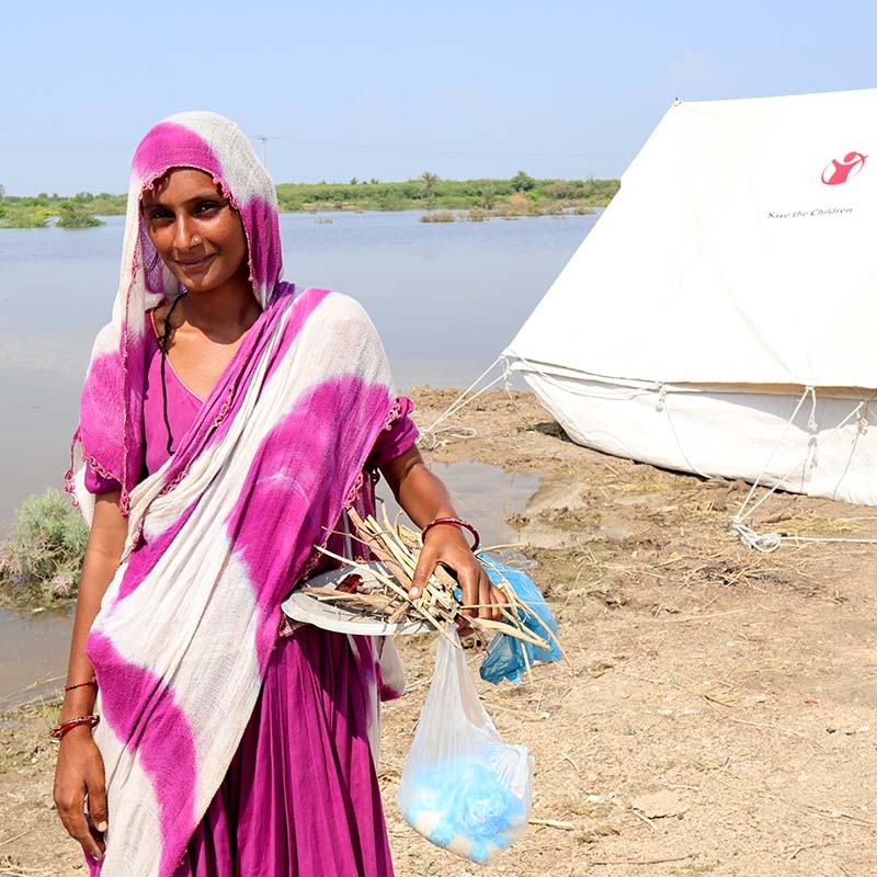 In Pakistan, a woman who lost her home in the dealdy flooding stands near a temporary shelter provided by Save the Children.