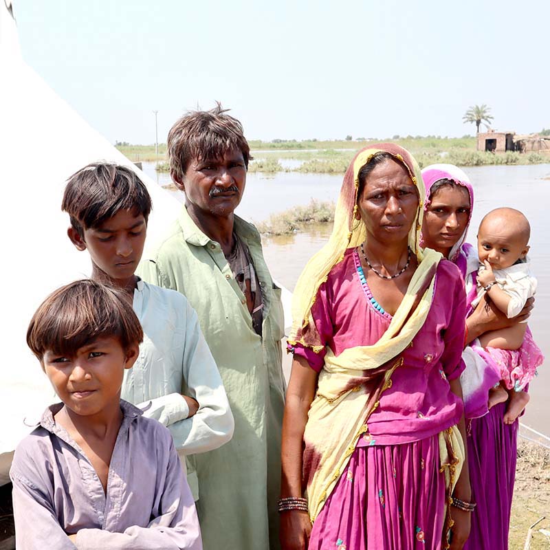 In Pakistan, a family stands near flooded water and a makeshift shelter provided by Save the Children. 