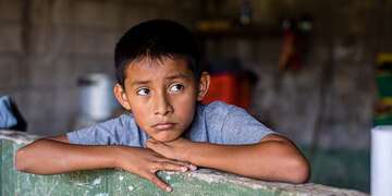 11-year-old Anderson rests his head on his hands while sitting inside his home in El Salvador.