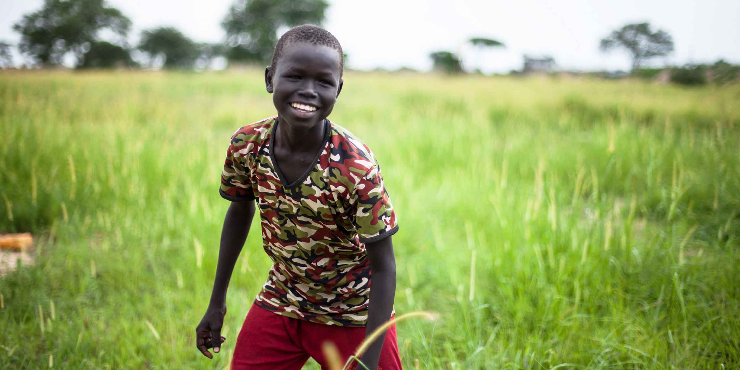 A boy stands smiling in a field. 