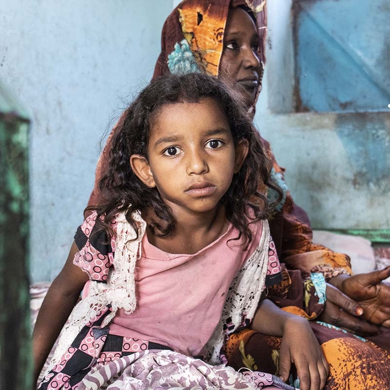 In Sudan, an 8-year old girl sits with her mother while receiving health care for cholera.