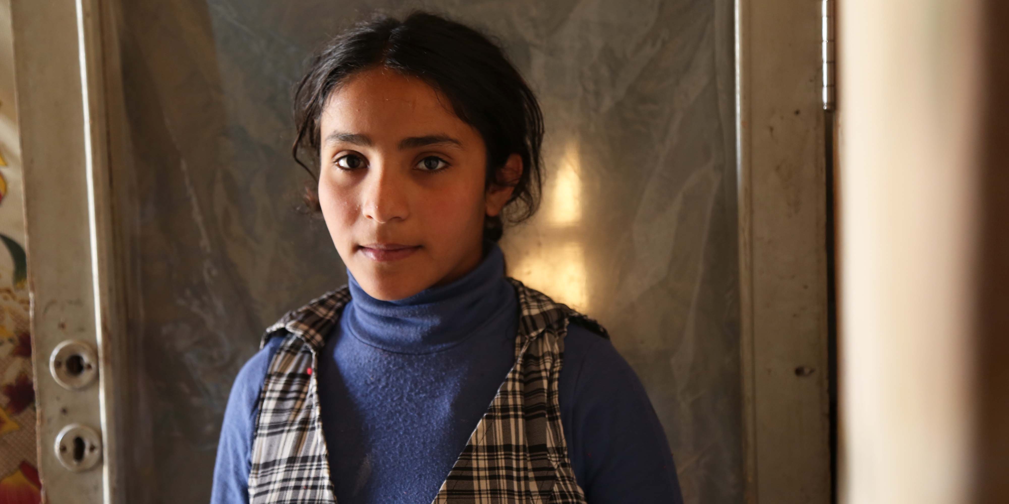 Syria, a girl in a blue turtleneck looks into the camera
