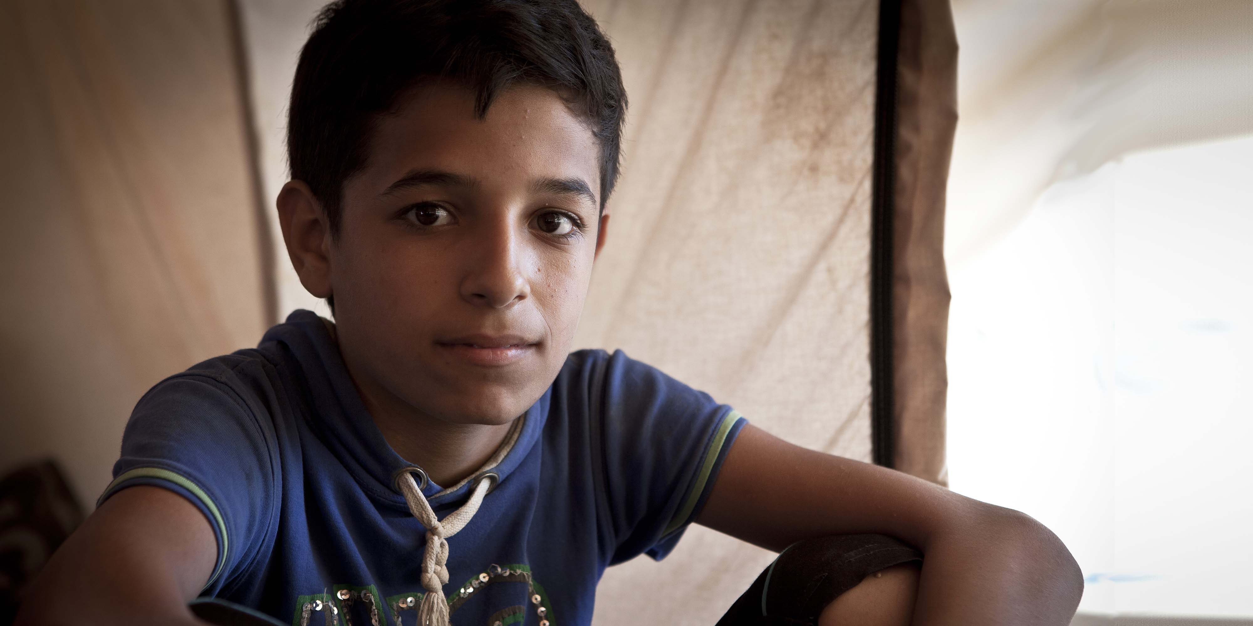 Syria, a young boy in a blue shirt looks into the camera