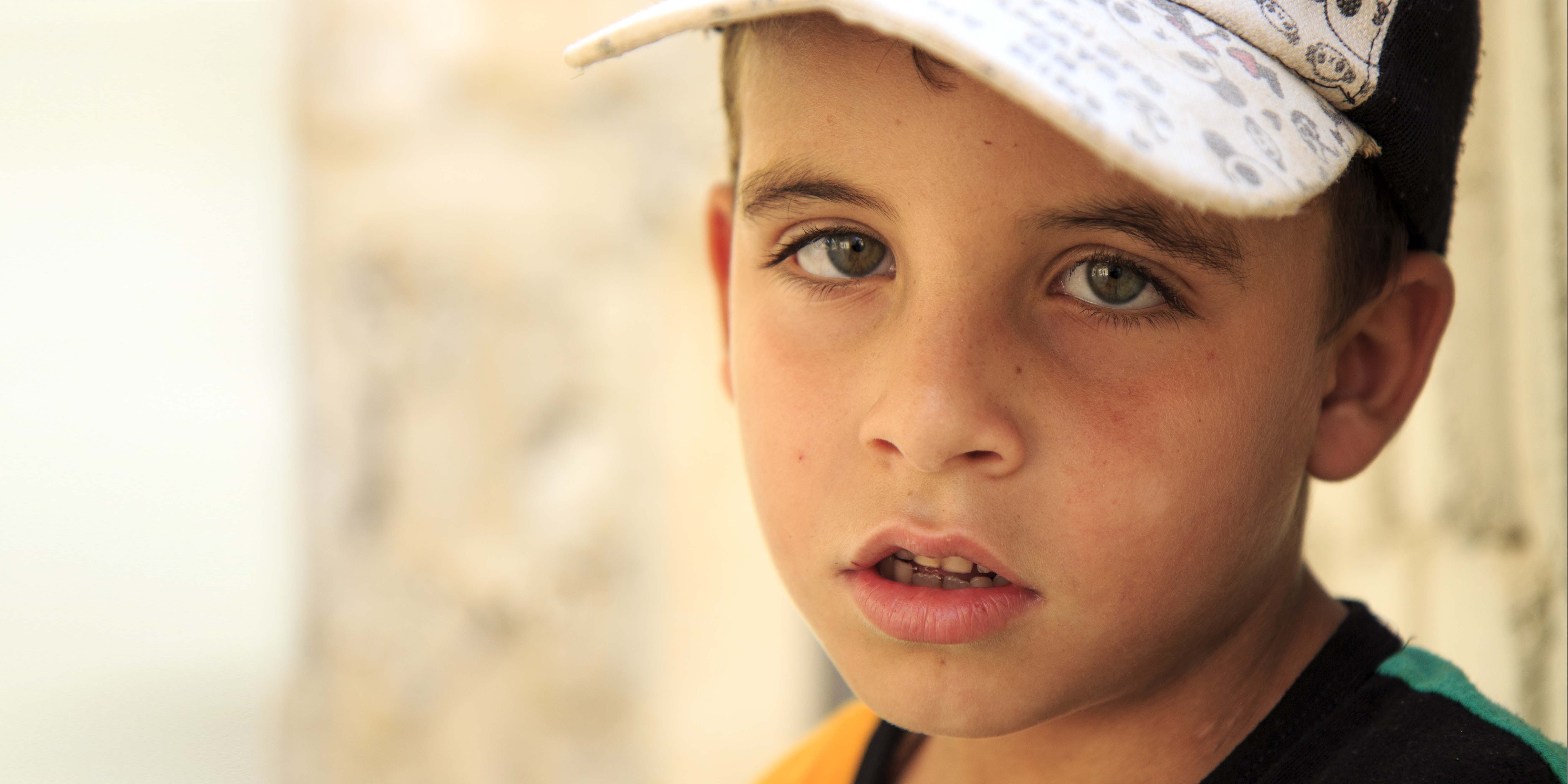 Syria, a little boy in a baseball cap looks into the camera