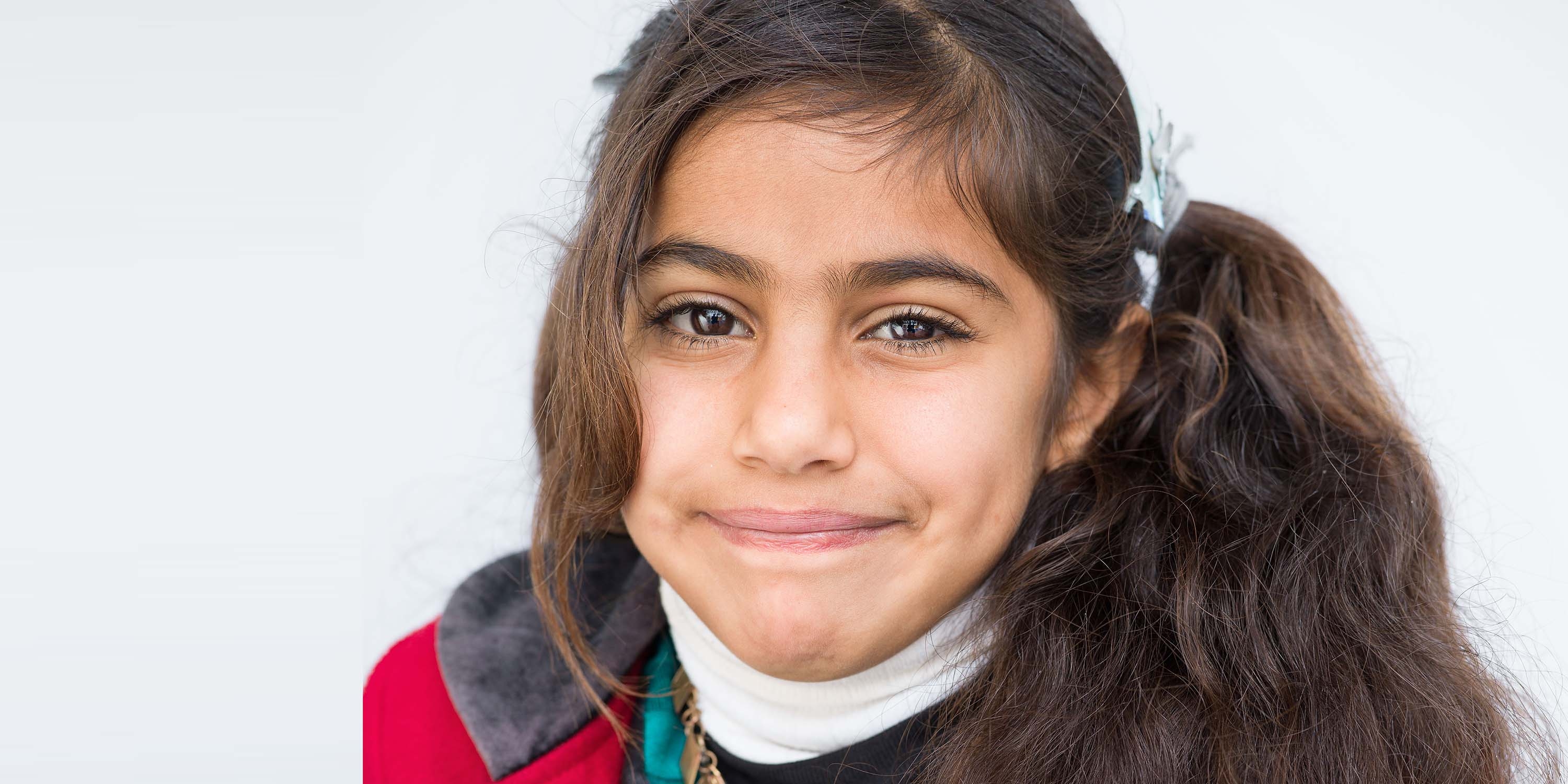 Syria, a 7 yr. old girl with a side ponytail smiles at the camera