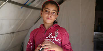 Syria, a young girl in a pink hoodie and pink headband looks at the camera