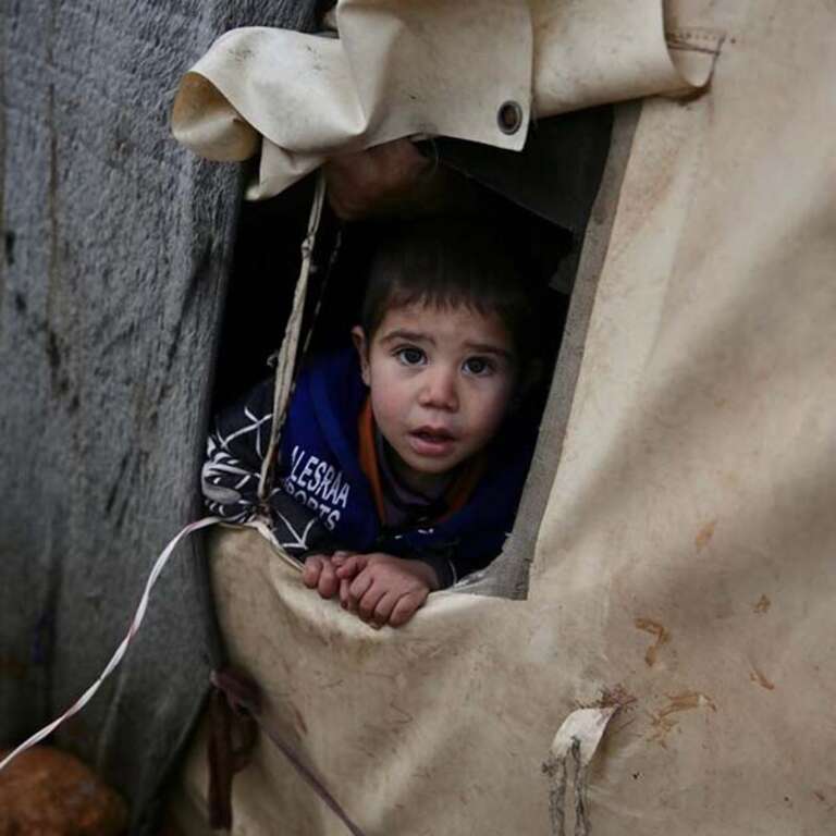 A four-year old refugee boy looks out from a tent set up in a camp in Syria for displaced children and families. 