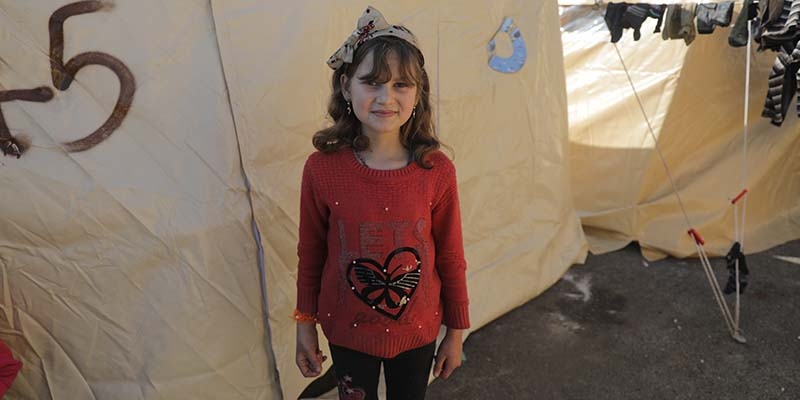 In Syria, where deadly earthquakes have displaced millions, a girl stands in front of a temporary shelter.