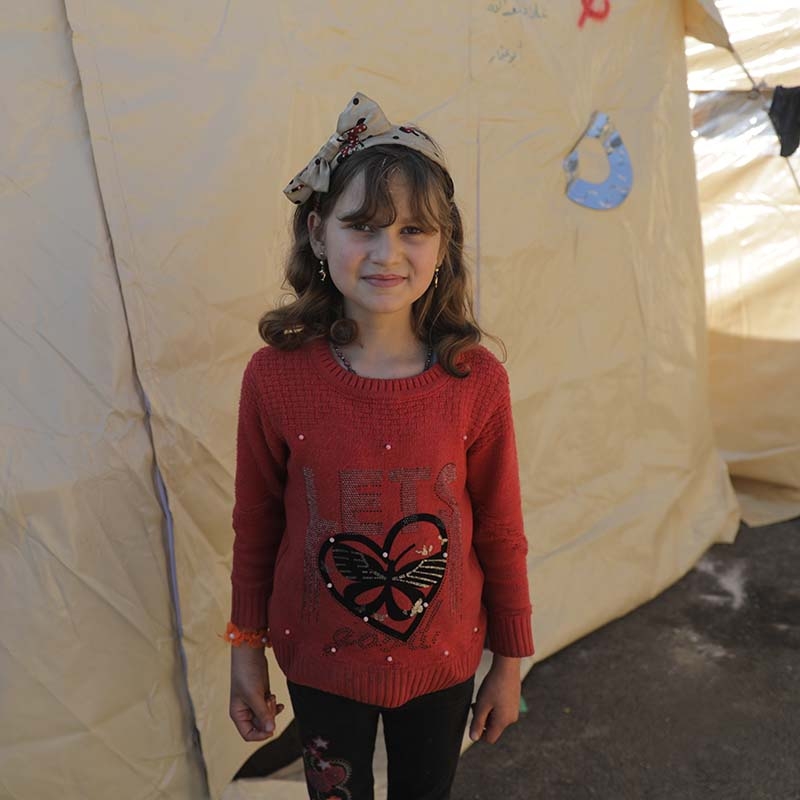In Syria, a girl stands in front of a temporary shelter for those displaced by recent earthquakes.
