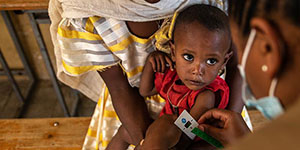 A two-year old sits on his mother's lap while receiving a vitamin supplement at mobile health clinic in Ethiopia where Ethiopian refugees now live.