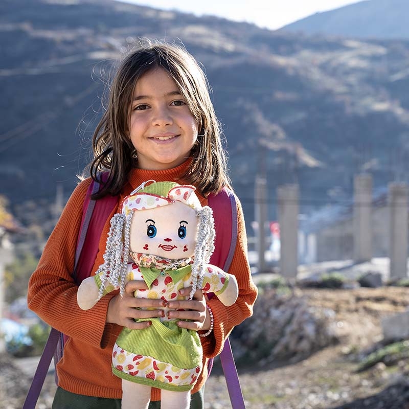 In Turkey, a 9-year old girl smiles while holding a doll she received as part of the recovery efforts following the 2023 earthquake.