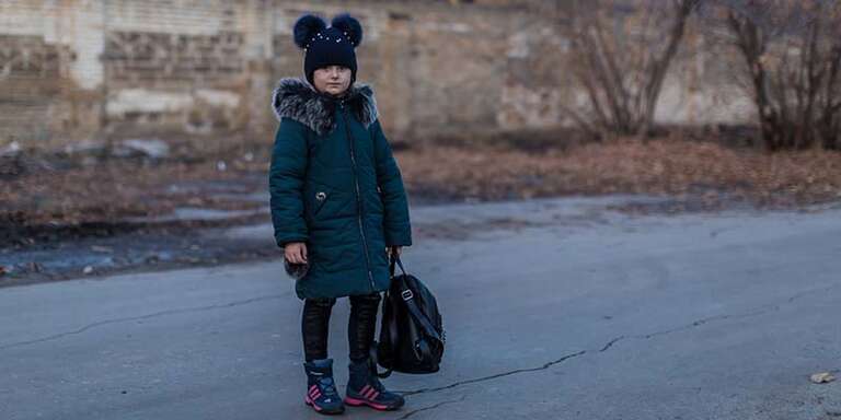 In Ukraine, a girl stands alone against a dark street with crumbling brick. 