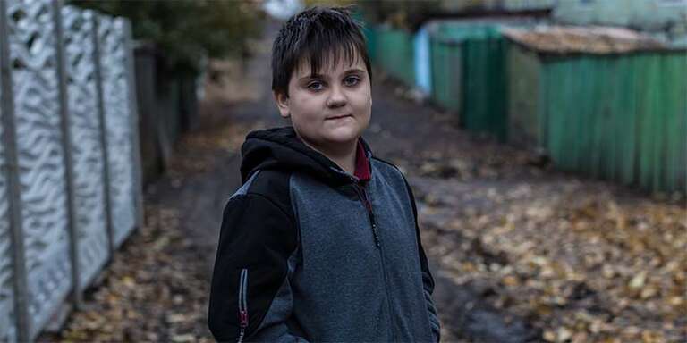 In Ukraine, a boy stands alone against a dark background.