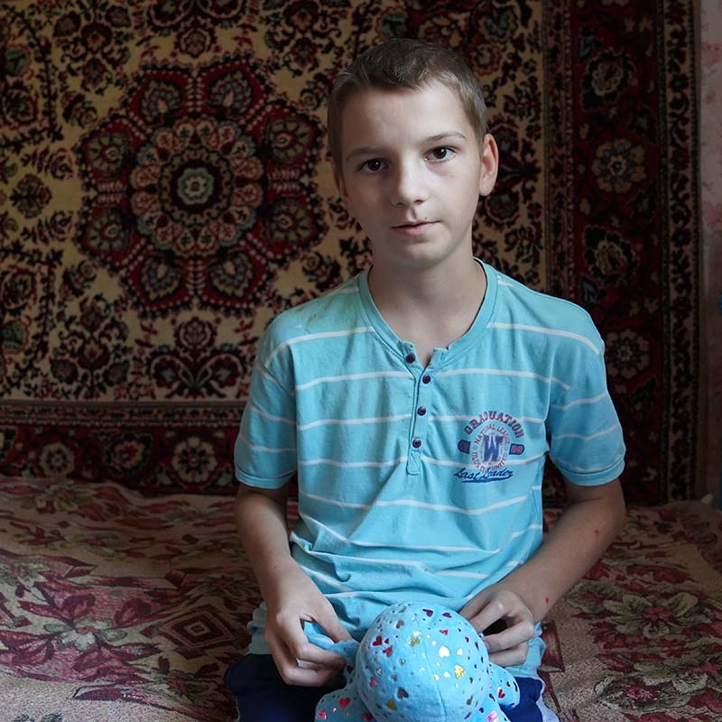 A young boy, whose family was displaced by the conflict in Ukraine, sits on his bed holding a stuffed animal. 