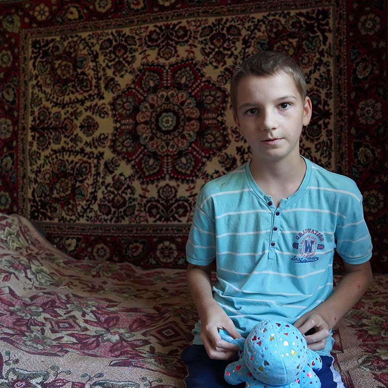 A young boy from Ukraine who fled the conflict sits on a bed holding a stuffed animal. 