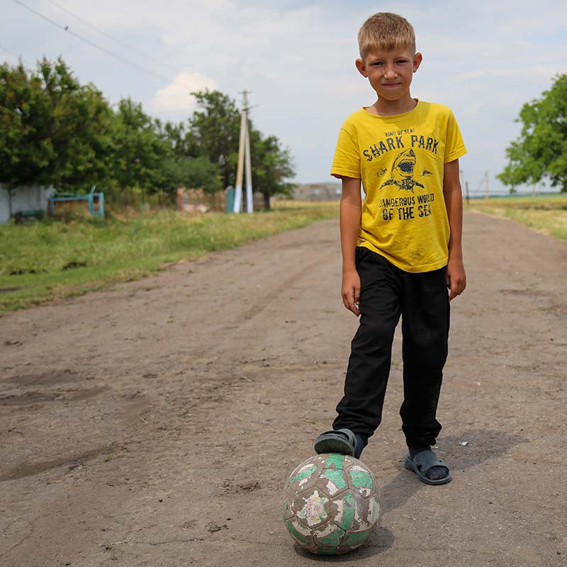 A young boy stands on a dirt road in Ukraine, where cluster mines are putting children at grave risk.