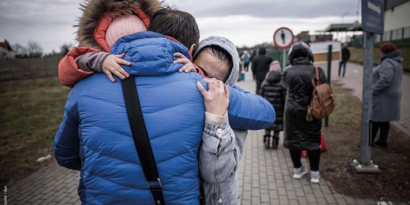In Ukraine, a girl wears a coat while standing in line with others who have been forced to flee due to conflict. 