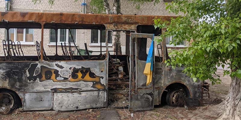 In Ukraine, a bus that has been destroyed by the war sits outside a damaged school building. 