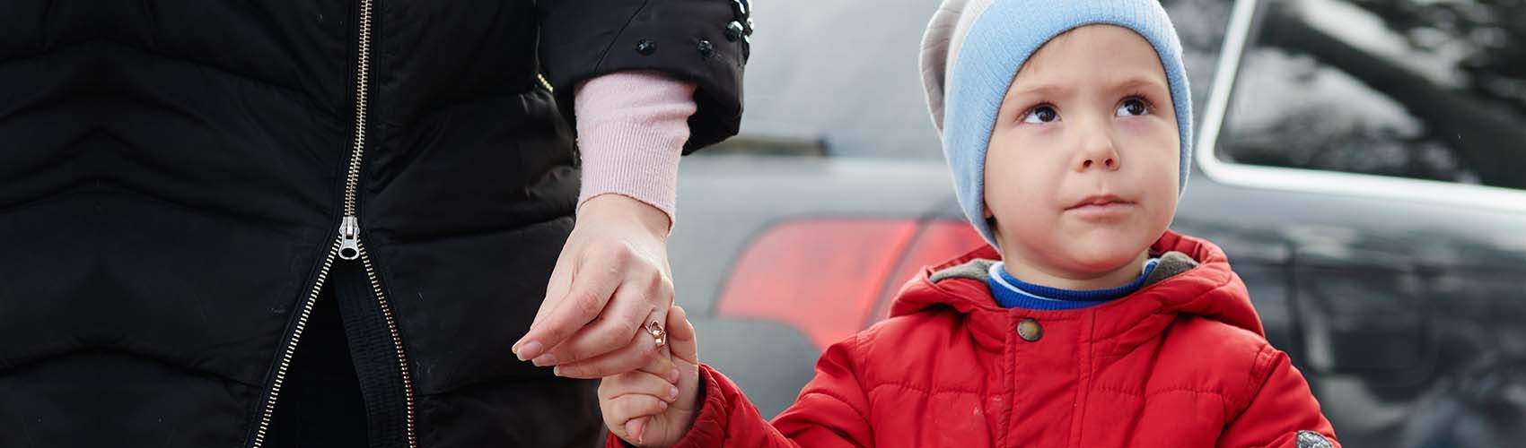 A Ukrainian boy wears a hat and coat while holding his mother's hand as the pair stands outside. 