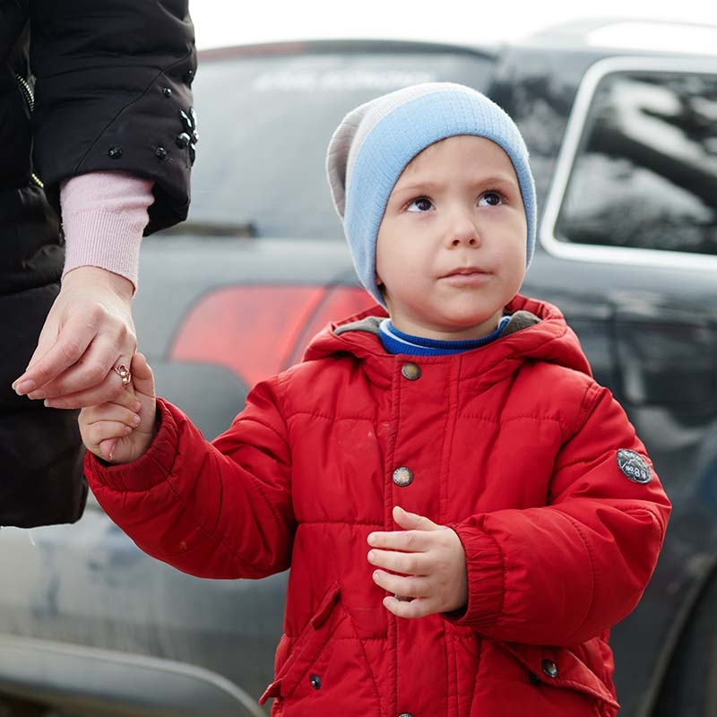 A Ukraine boy wears a coat and a hat while holding his mother's hand. 