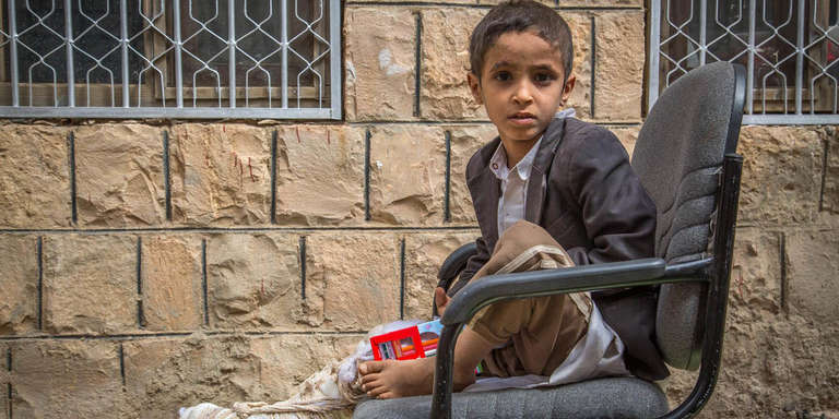 A boy whose leg was injured in an airstrike sits in a chair outside in Yemen.