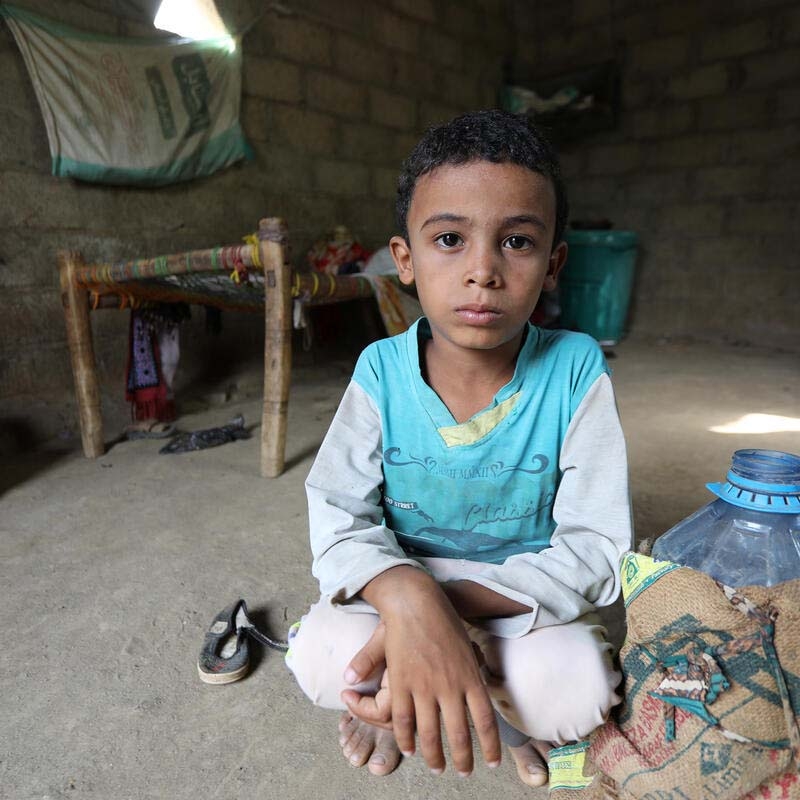 In Yemen, a boy kneels next to a water jug. 