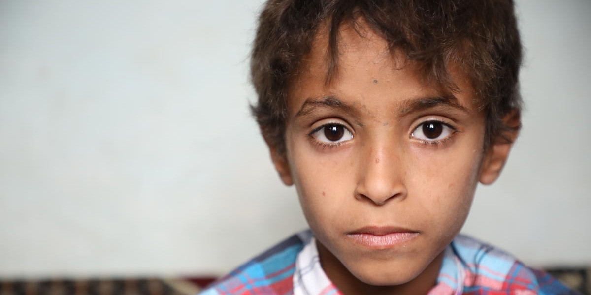 An eight-year old boy is pictured sitting inside a home in Yemen. The boy was on a school bus riding through Saada, Yemen, when the bus was bombed. 40 children under the age of 10 were killed. He survived but not without significant injuries. He had shrapnel fragments next to his eye, in his leg and in his little toe. His foot was broken. Save the Children helped provide the boy with medical care and now, his physical injuries have healed. Since May 2015, through donor support, Save the Children has reached more than 2 million children with lifesaving assistance. Photo credit: Sami M. Jassar / Save the Children, July 2019.