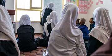 In Afghanistan, a female teachers stands in front of a room filled with girls and boys. 