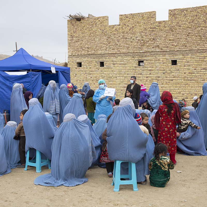 In Afghanistan, a group of women and children wait at an outdoor mobile health clinic.