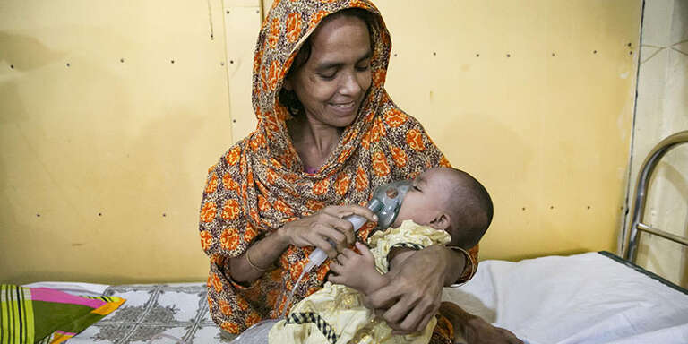 A mother smiles while giving a nebulizer treatment to her baby. 
