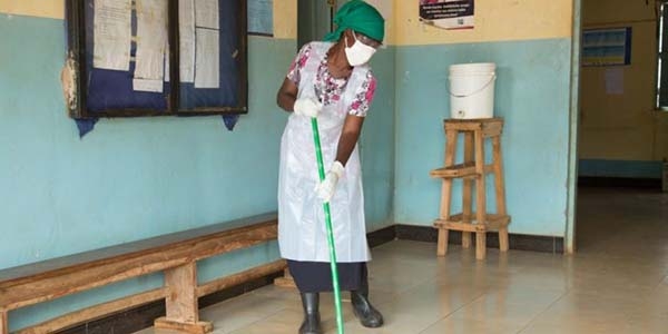 A woman cleans the floor of a health center while wearing gloves, an apron and a mask. 