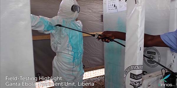 A man in a white jumpsuit is sprayed down wish a blue wash to disinfect against ebola. 