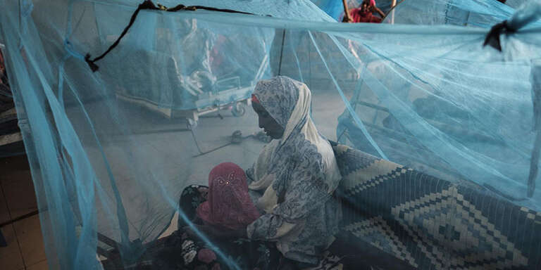 A woman in Ethiopia holds her child and is sitting under a blue mosquito net