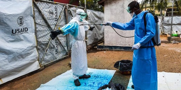 A health worker in a blue gown applies Highlight, a blue dye, to a fellow worker to decontaminate their protective garments from Ebola. 