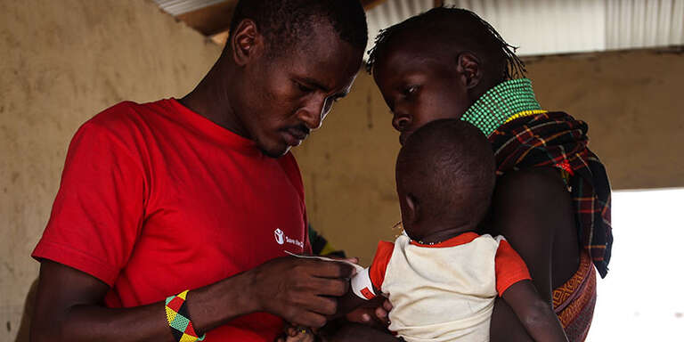 A Save the Children staff member attaches a MUAC band to a small child, who is being held by their mother.