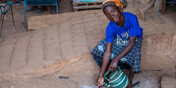 A 12-year-old girl wearing a blue t-shirt, orange scarf around her head and a colorful skirt washes her hands outside of her family home in Mali. Thanks to Save the children, the community the girls lives in has access to clean water and the children in the community understand the importance of living a healthy lifestyle by washing hands and staying clean. Photo credit: Victoria Zegler | Save the Children, Nov 2016.