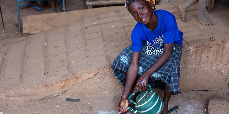 Mali, a girl in a blue t-shirt washes her hands and smiles at the camera