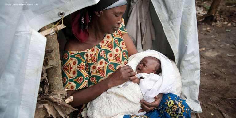 A woman sits under a tent and feeds her newborn.