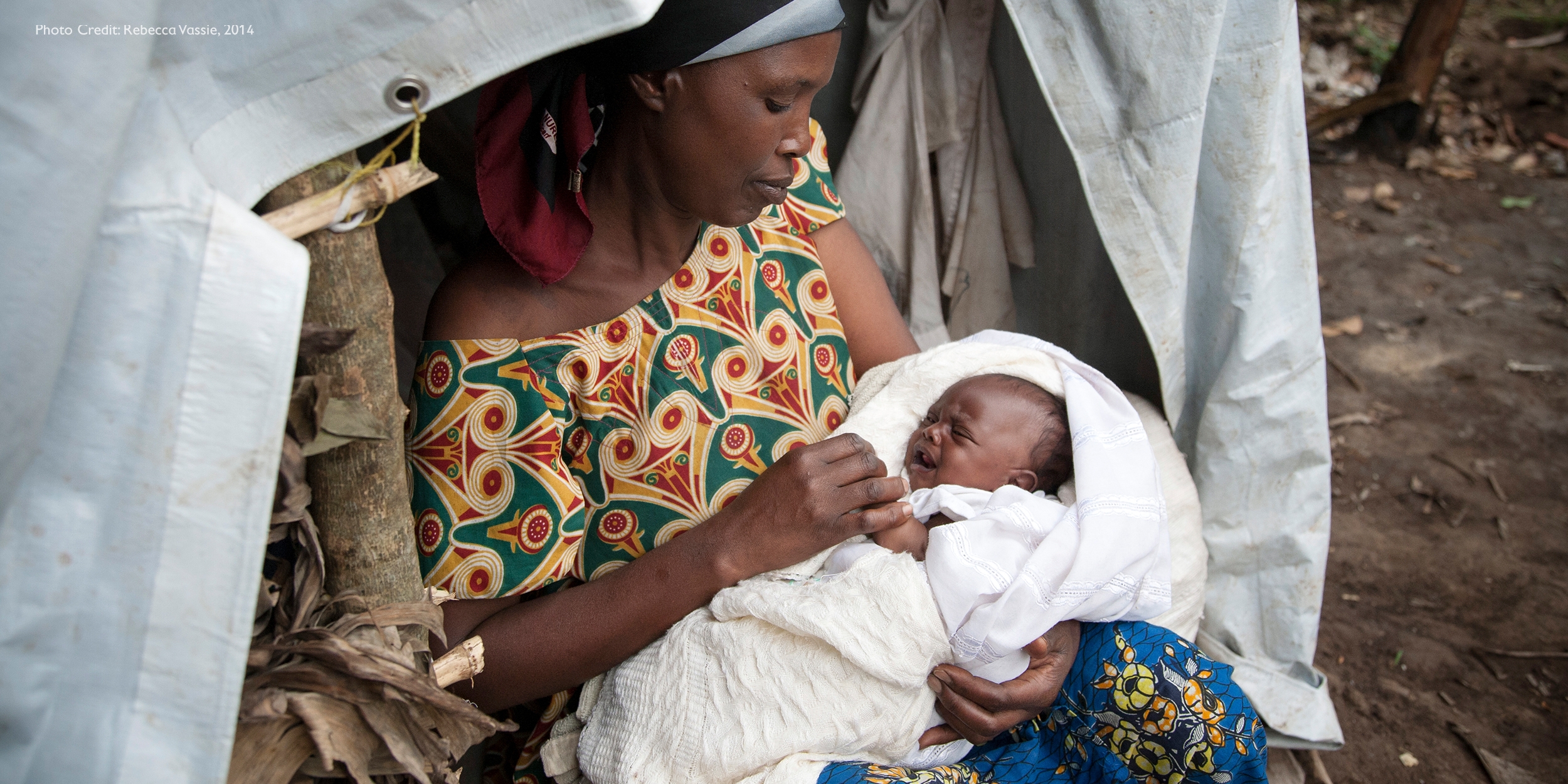 A woman sits under a tent and feeds her newborn.