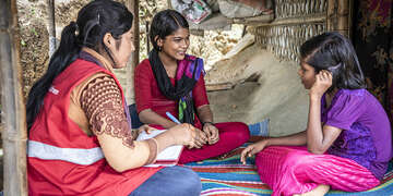 A Save the children staff member sits with two teenage girls. 
