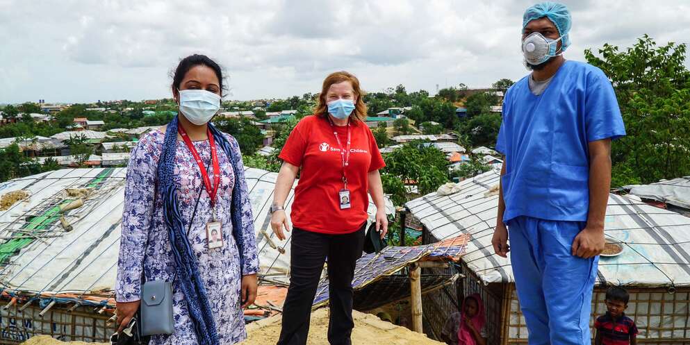 A group of three health care workers stand on a hill and wear face masks in Cox's Bazar refugee camp in Bangladesh.