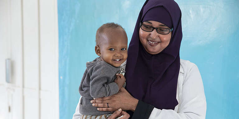 Both smiling, a doctor holds a young child.